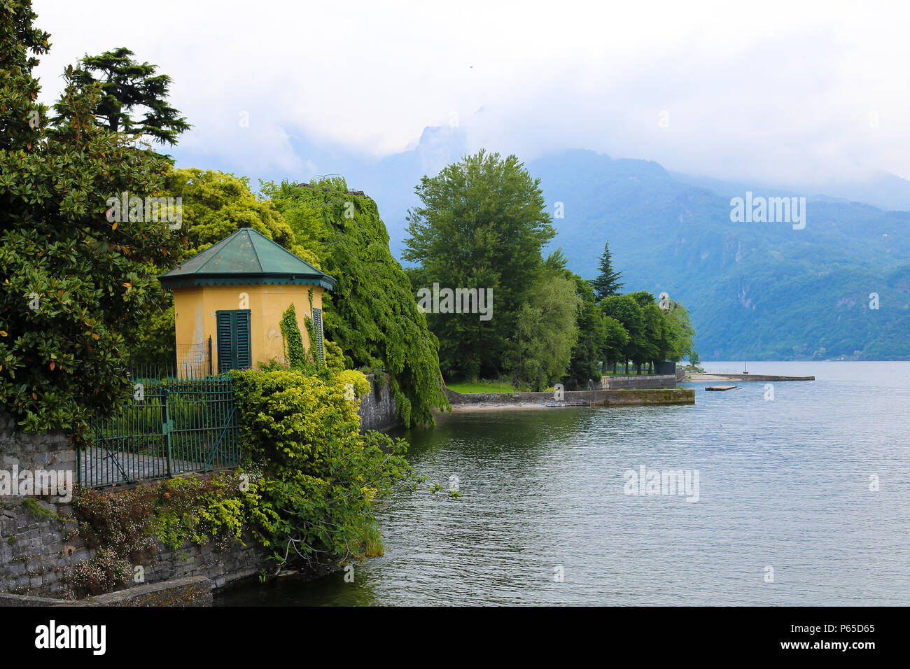 Grüner Zaun mit Efeu mit litle Gebäude in der Nähe des Comer Sees, mouintain im Hintergrund. Stockfoto