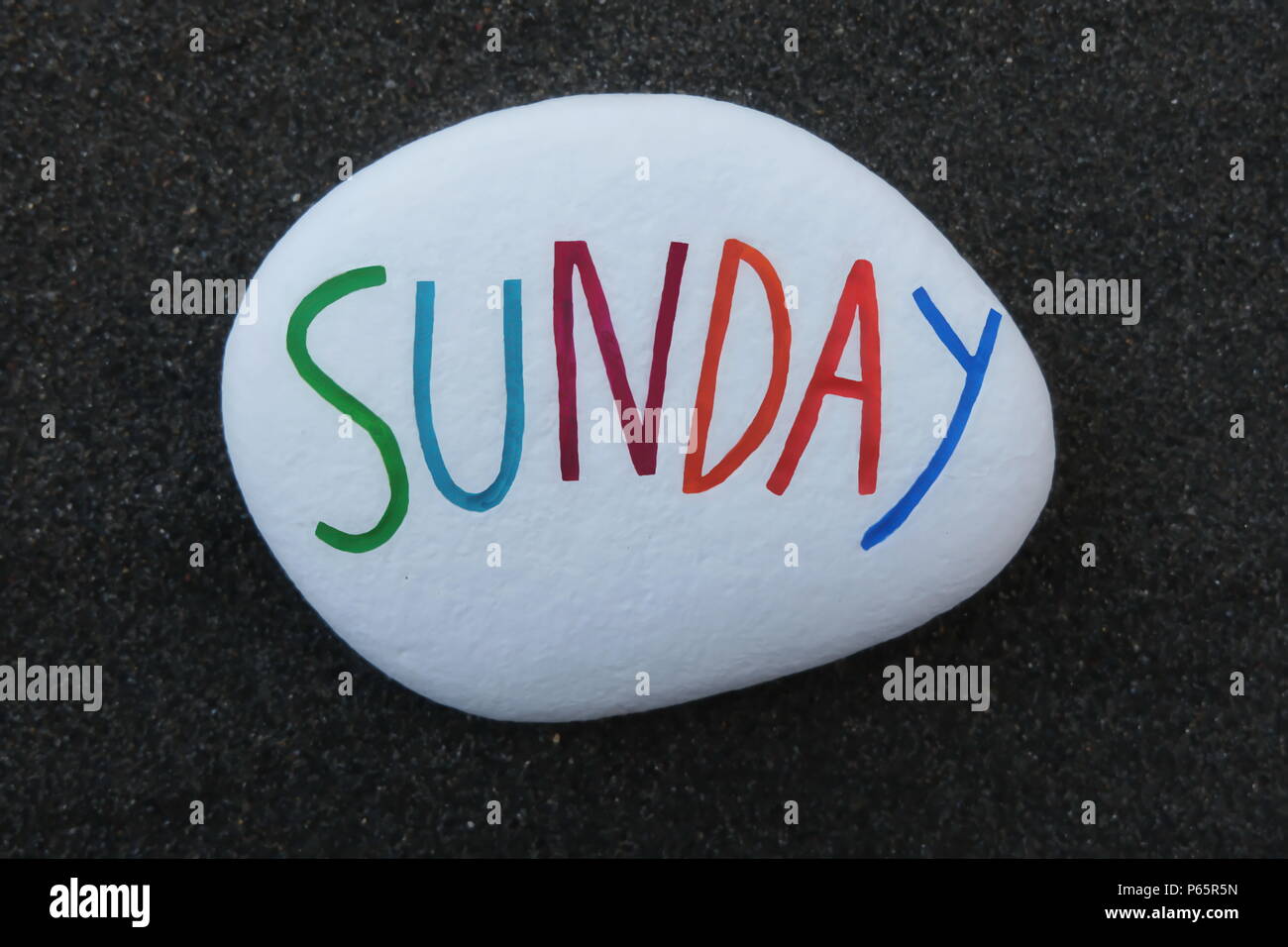 Sonntag, siebter Wochentag, auf einen weißen Stein über schwarzem vulkanischen Sand gehauen und gemalt Stockfoto