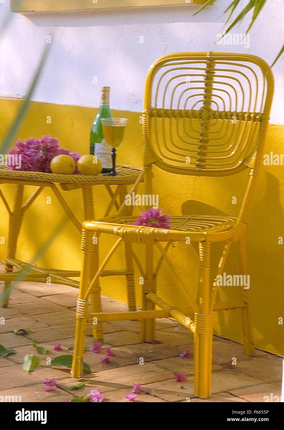 Der still-life Gelb lackiert Zuckerrohr Stuhl und tablewith Lila bougainvillea Stockfoto