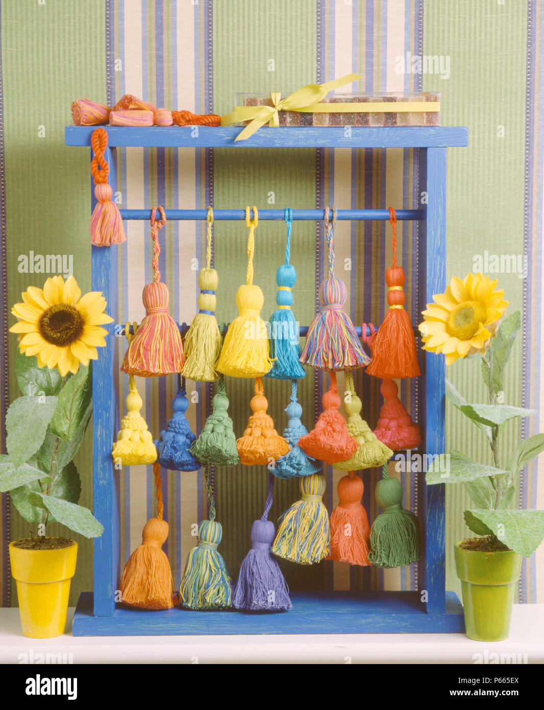 Nahaufnahme der Töpfe mit Sonnenblumen mit bunten Baumwoll Quaste an blauer Rahmen, mit einer einfachen Skulptur Stockfoto