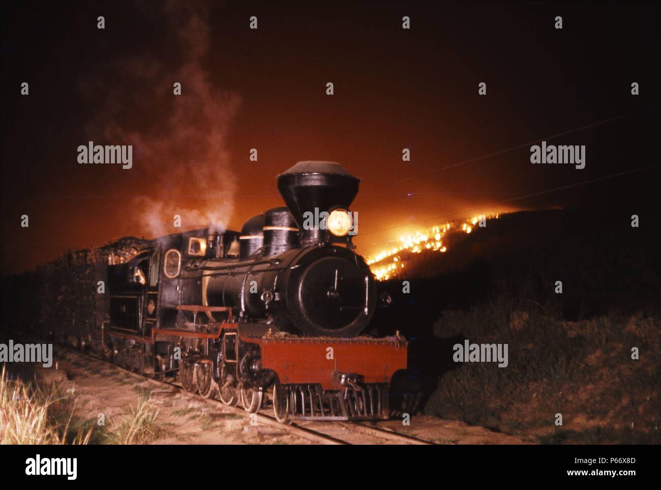 Eine typisch britische 4-6-0 von Robert Stephenson in Newcastle Upon Tyne 1906 erbaut, führt ein Zug durch brennende Felder. In der Zuckerplantage service Stockfoto