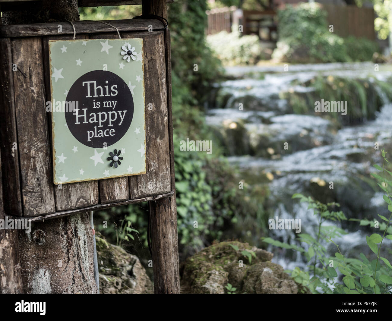 "Dies ist mein glücklicher Ort "motivierende Schild hängen in einem wunderschönen Garten mit einem kleinen Wasserfall im Hintergrund. Stockfoto
