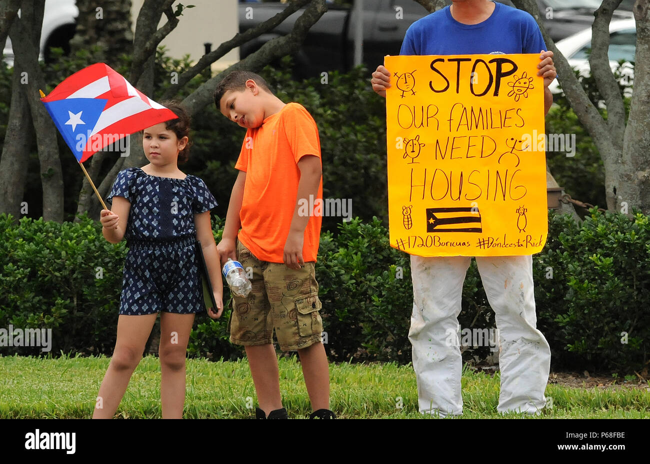 Kissimmee, Florida, USA. 28 Jun, 2018. Ein junges Mädchen Wellen ein Puerto Rican flag wie Sie, ihr Bruder und ihr Vater, Erie Salgado (rechts), die von den Hurrikanen Irma und Maria im September 2017 in Puerto Rico vertrieben wurden, zeigen eine Unterstützung für die Wohnung aus Florida reg zu verlangen. Rick Scott in Kissimmee, Florida am 28. Juni 2018. Die Familie lebt in einem lokalen Holiday Inn seit November 2017 unter der FEMA Hotel Voucher Programm endet am 30. Juni. Insgesamt 630 Familien, die 1720 vertriebenen stehen vor Vertreibung, sobald das Gehäuse Hilfe abgeschnitten wird. Credit: Paul Hennessy/Alamy leben Nachrichten Stockfoto