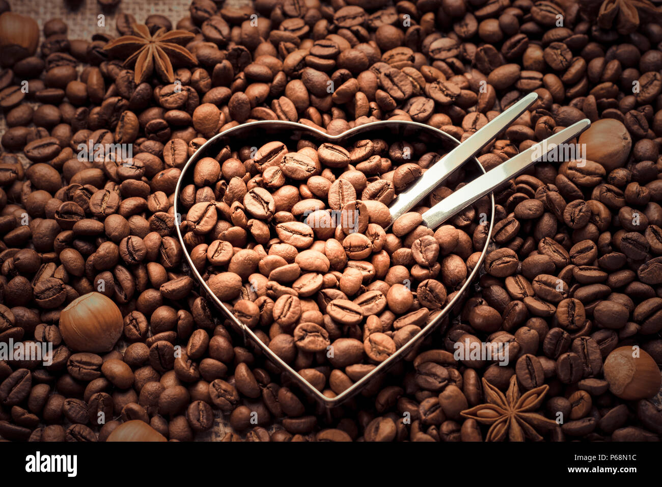 Herzerwärmend. Kaffee Bohnen und Nüsse Hintergrund mit einem Metal Heart Form in einem nahen - Ansicht von oben Stockfoto