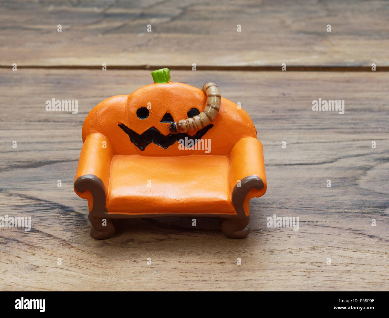 Super oder riesigen Wurm kriecht auf orange Miniatur Keramik Kürbis Couch oder Sofa über dunklen Holz- Oberfläche mit Kopie Raum als Hintergrund in Halloween, Ornament, Feier, und Dekoration Stockfoto