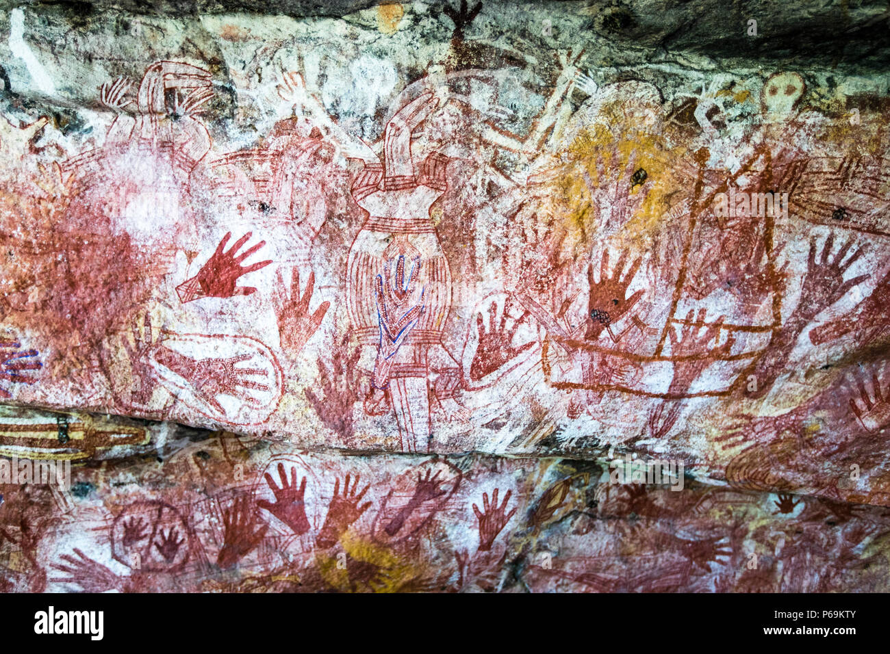 Eine dichte Galerie von Handabdrücken und menschenähnlichen Figuren in Roter Ocker, Weiß und Blau bedeckt einen Felsvorsprung nahe Mount Borradaile, West Arnhem, Northern Territory, Australien; das Weiß wurde mit dem Mund auf den Felsen gesprüht, das Blau stammt von Reckitt's Blue, einem Waschmittelzusatz, der früher aus Ultramarin und Natron hergestellt wurde. Stockfoto