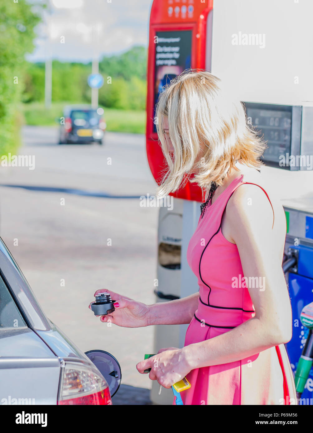 Weiß, attraktive kaukasisch Weiblich 29 Jahre alt mit blonden Haaren, in rosa Kleid, schließen Auto Tank mit Stecker nach dem Tanken an der Tankstelle. Stockfoto