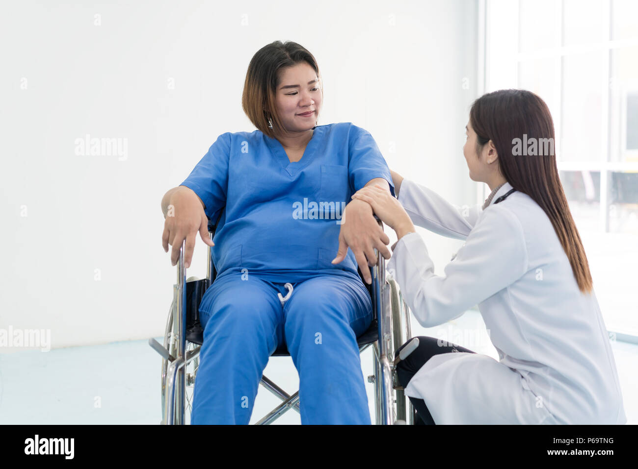 Asiatische Frau Doktor im Gespräch mit jungen schwangeren Frau im Rollstuhl im Krankenhaus. Schöne asiatische Arzt darauf achten, dass der Patient im Rollstuhl. Stockfoto