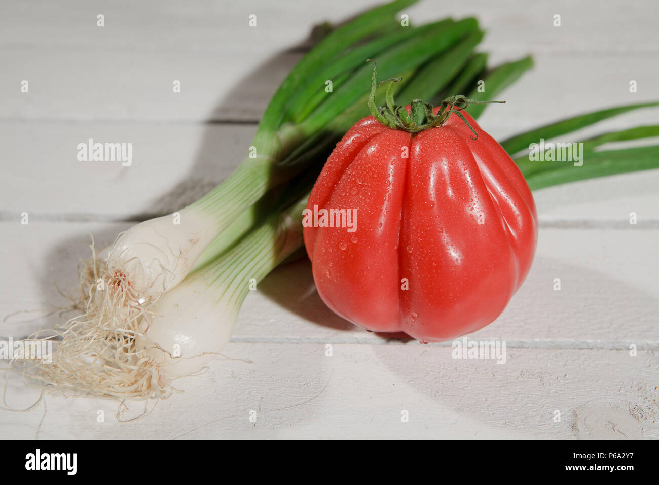 Frische, grüne Zwiebeln und Buffalo Herz Tomate auf weißen Garten Tisch, in der Nähe Stockfoto