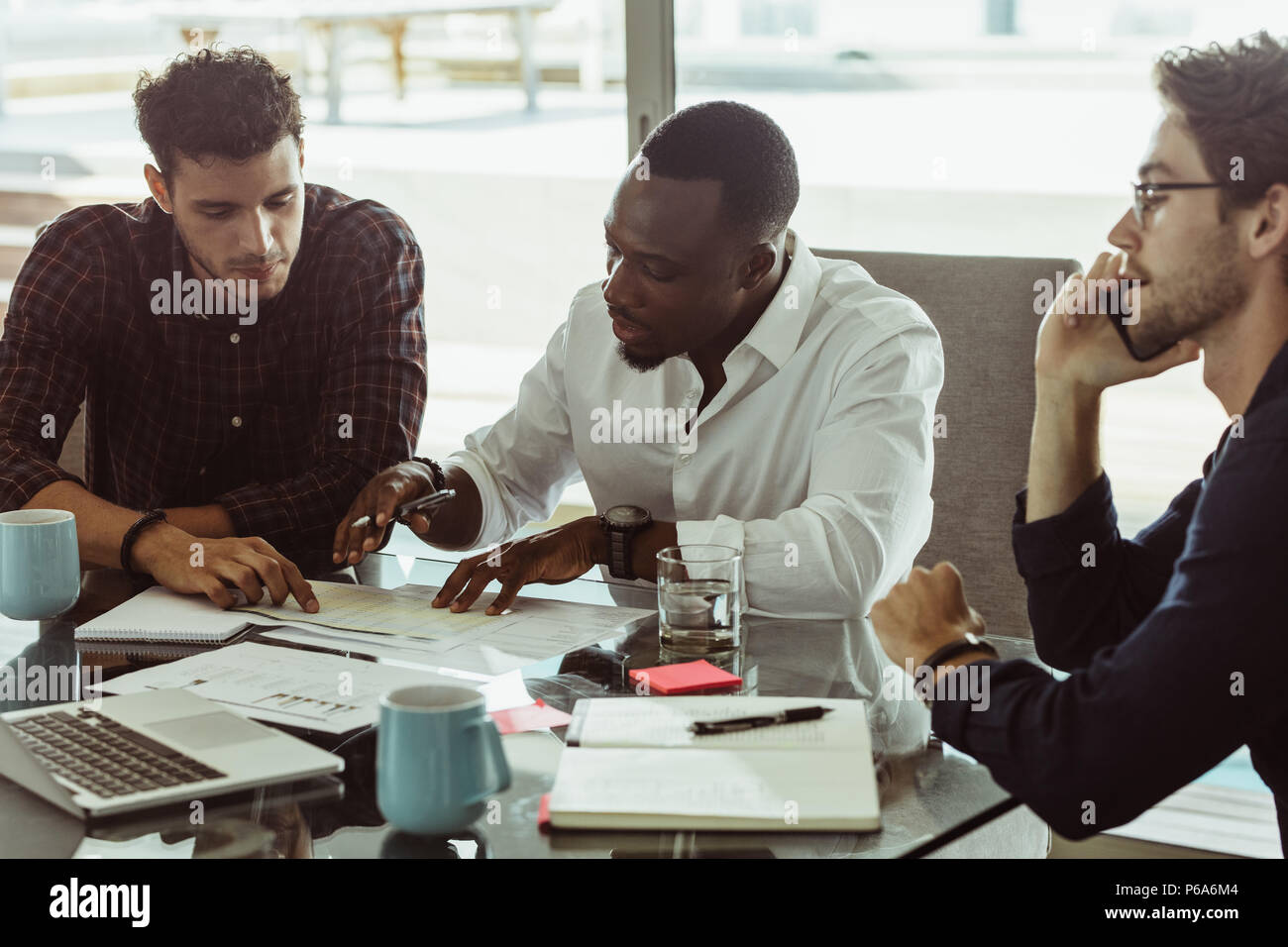 Unternehmer diskutieren Arbeit am Konferenztisch Sitzen im Büro. Zwei Männer diskutieren, arbeiten, während ein anderer Mann Gespräch am Handy ist. Stockfoto