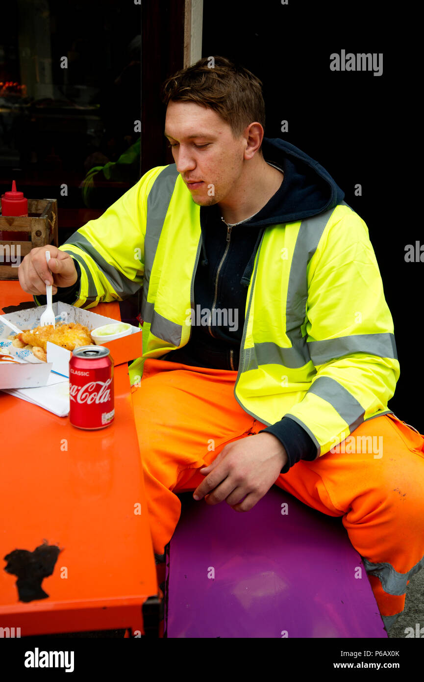 Hackney. Broadway Markt. Einen rumänischen Bauarbeiter in fluoreszierenden Schutzkleidung isst Fisch und Chips für das Mittagessen. Stockfoto
