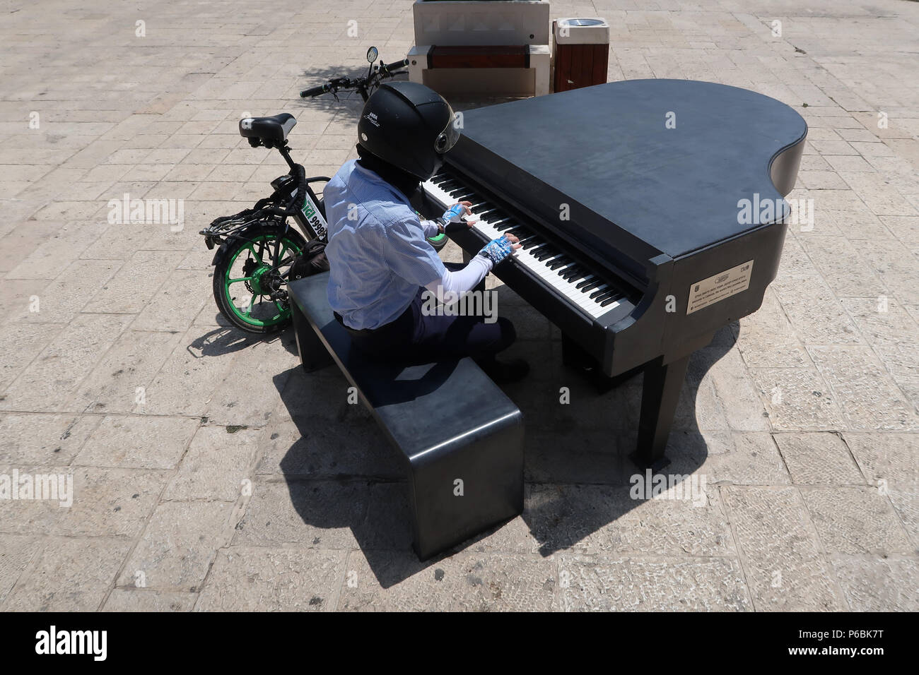 Eine Person, die einen Rollerhelm trägt, spielt Klavier aus Beton im Freien, West-Jerusalem, Israel Stockfoto