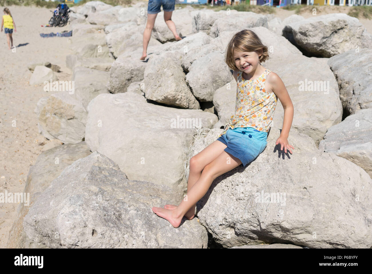 Weibliches Kind sitzen auf den Felsen am Strand Stockfoto