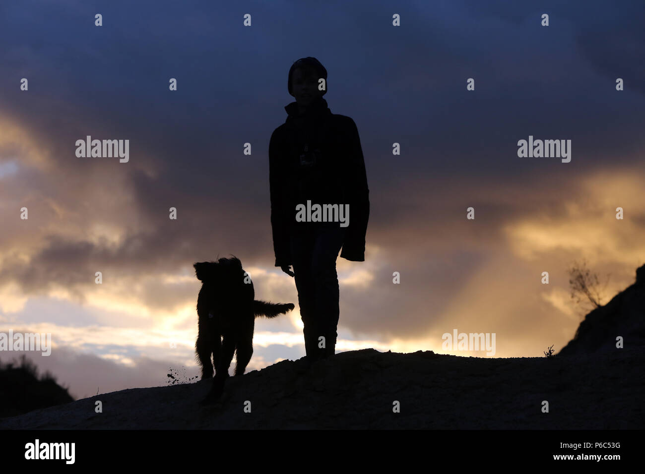 Wustrow, Deutschland - Silhouette, Boy steht mit seinem Hund auf einer Düne Am Abend Stockfoto