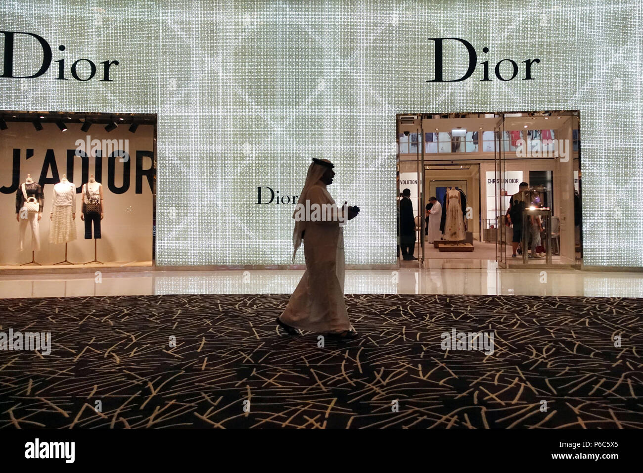 Dubai, Vereinigte Arabische Emirate, Mann in Tracht Spaziergänge hinter einem Christian Dior Zweig Stockfoto