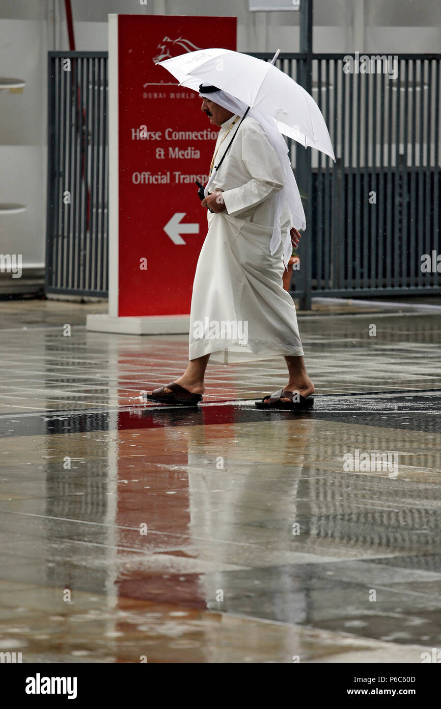 Dubai, Mann in arabischen Kostüm, läuft unter seinen Schirm im Regen Stockfoto