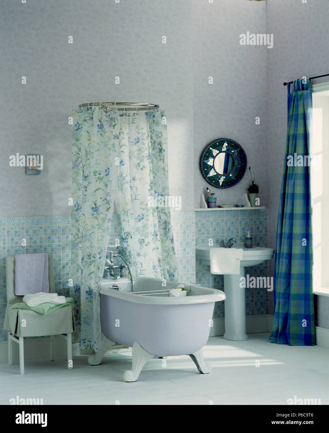 Weiß rolltop Badewanne mit Duschvorhang mit Blumenmuster in der Mitte des weißen Badezimmer mit blau karierte Vorhänge und weiß Bodenbeläge Stockfoto