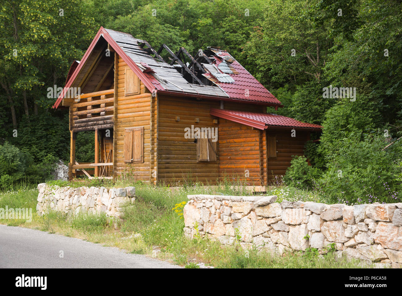 Schlecht verlassene Feuer Holzhaus mit klaffende Loch im Dach am Berghang an Njeguši über Kotor, Montenegro mit grünen Bäumen im Hintergrund beschädigt. Stockfoto