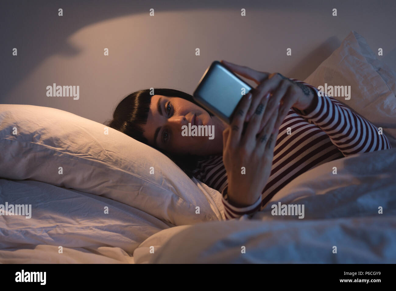 Frau mit Handy im Schlafzimmer Stockfoto