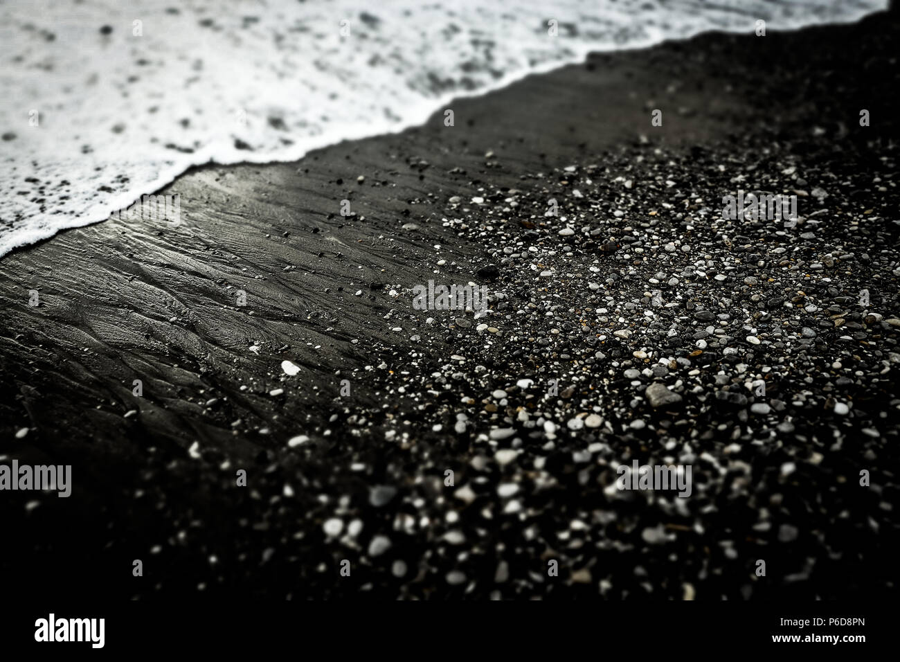 Sea Foam wave auf texturierte schwarzer Sandstrand mit kleinen Steinen. Schwarze und weiße dramatische Foto. Hintergrund Stockfoto