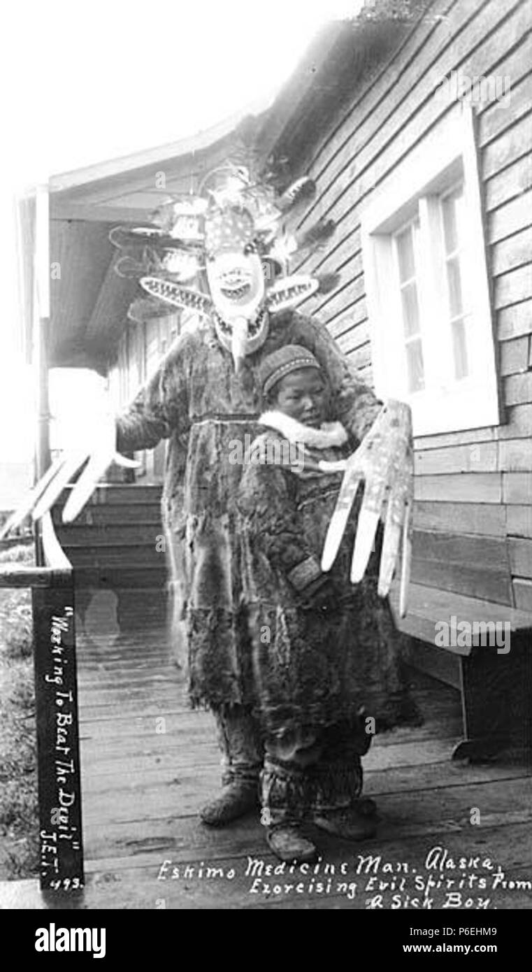 Englisch: Aglegmiut Schamane in Kostüm, mit Boy, Ca. 1912. Englisch: Obwohl  durch die christlichen Missionare verboten, diese Masken und übergroßen  Hände waren immer noch hergestellt und in den frühen 1900er Jahren