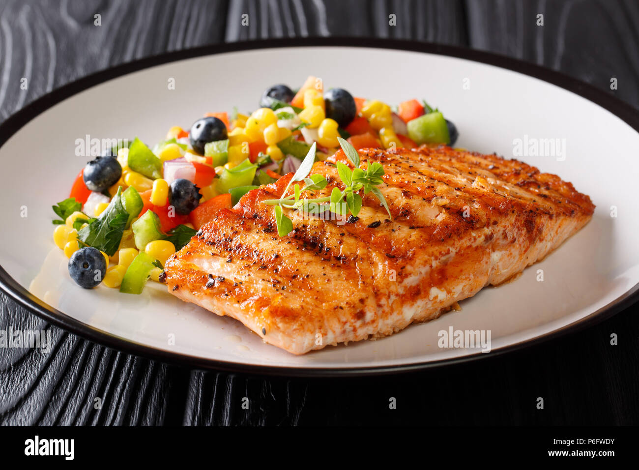 Gesundes Essen: gegrilltes Lachsfilet mit Paprika, Mais, Blaubeere und Zwiebel Salat closeup auf einem Teller auf den Tisch. Horizontale Stockfoto