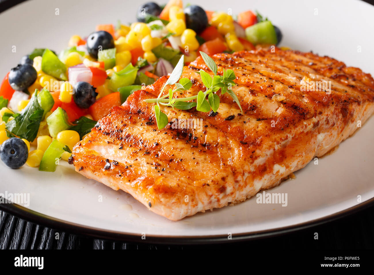 Gegrillter Lachs mit mexikanischen Salsa an Gemüse und Beeren close-up auf einem Teller auf dem Tisch. Horizontale Stockfoto