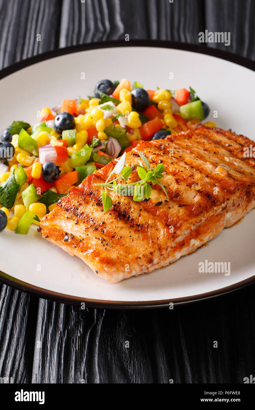 Gegrillter Lachs mit Salat Salsa an Gemüse und Beeren in der Nähe serviert auf einem Teller auf den Tisch. Vertikale Stockfoto