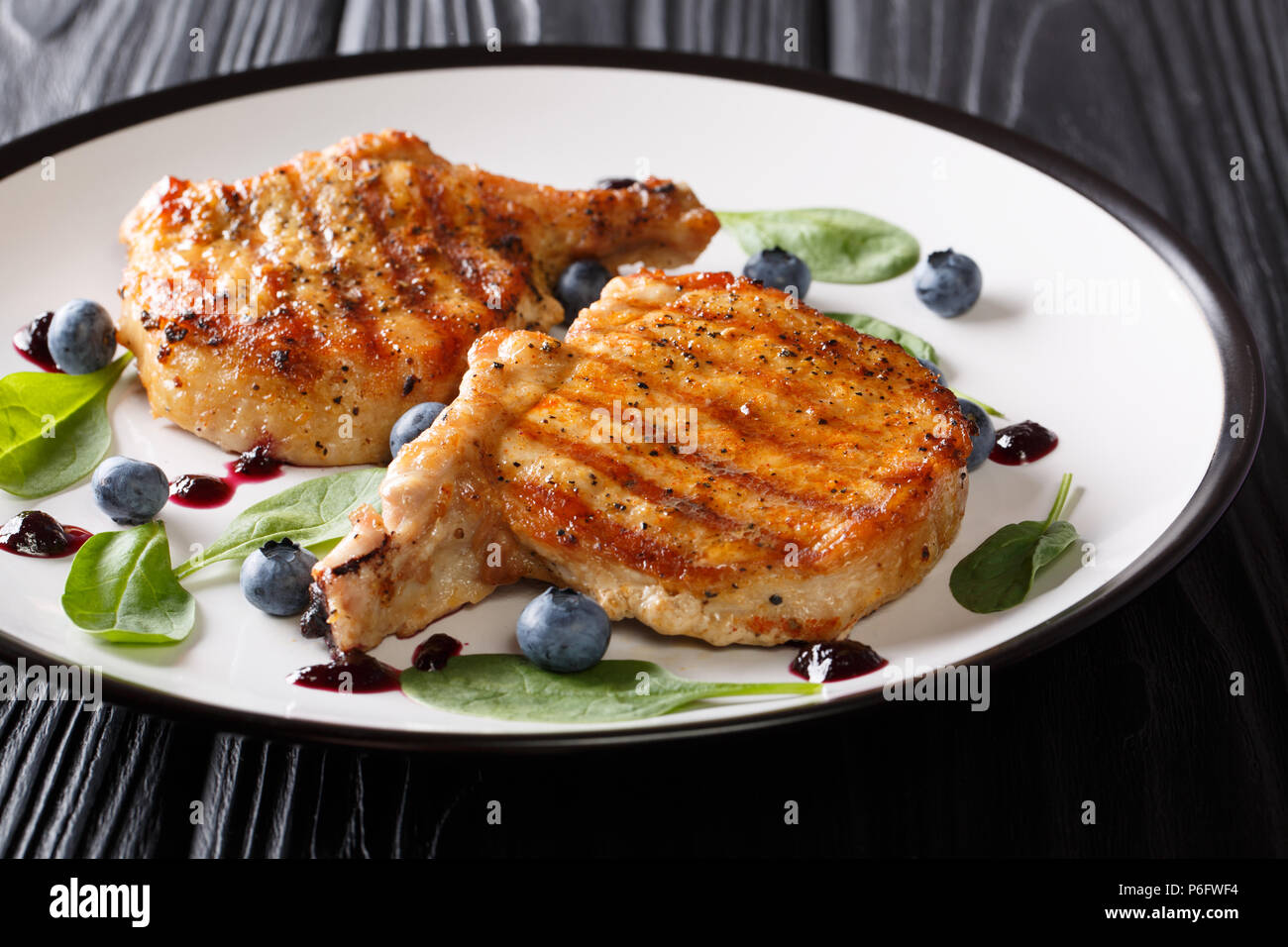 Grill essen: Gegrilltes Schweinesteak mit Rippen mit frischen Heidelbeeren Sauce und Spinat closeup auf einem Schild an einem Holztisch. Horizontale Stockfoto