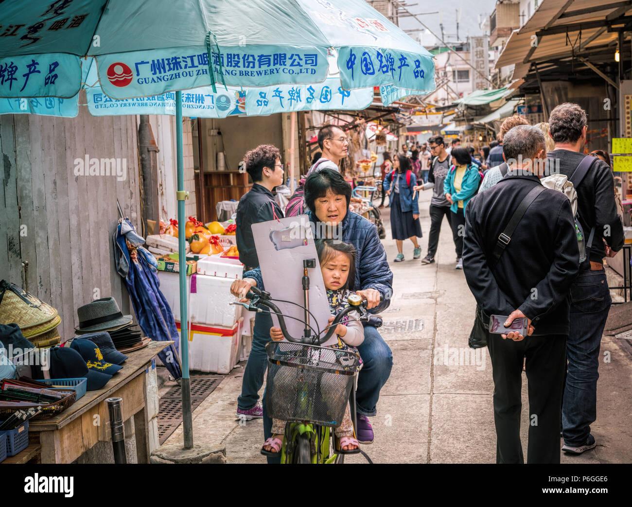 19. Februar 2018 - Lantau Island, Hong Kong. Asiatische Frau Radfahren in der Dorfstraße von Tai O mit Kind auf dem Fahrrad. Stockfoto