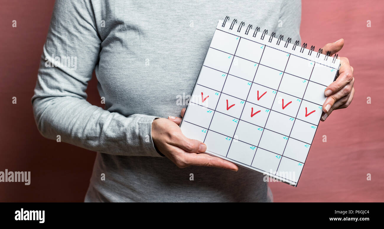 Eine Frau hält einen Kalender mit markierten Tagen. Ausrufezeichen symbolisieren die Verzögerung einer monatlichen, unerwünschten Schwangerschaft. Konzeptzeitraum. Stockfoto