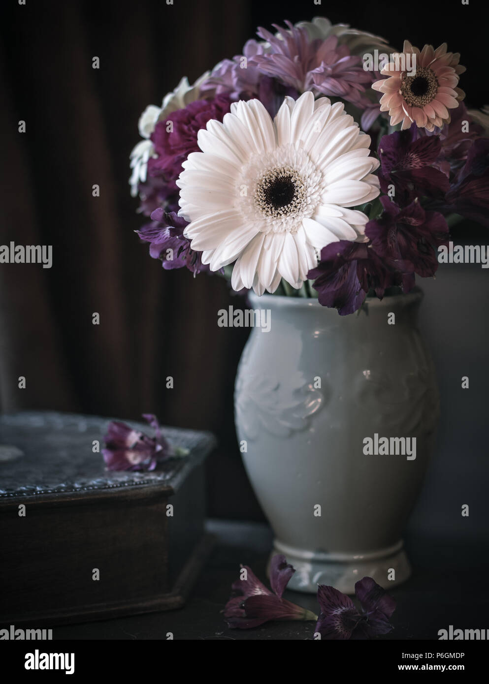 Dunkel gefärbte Blumen in einer Vase mit dunklem Hintergrund und gedeckten Farben. Stockfoto