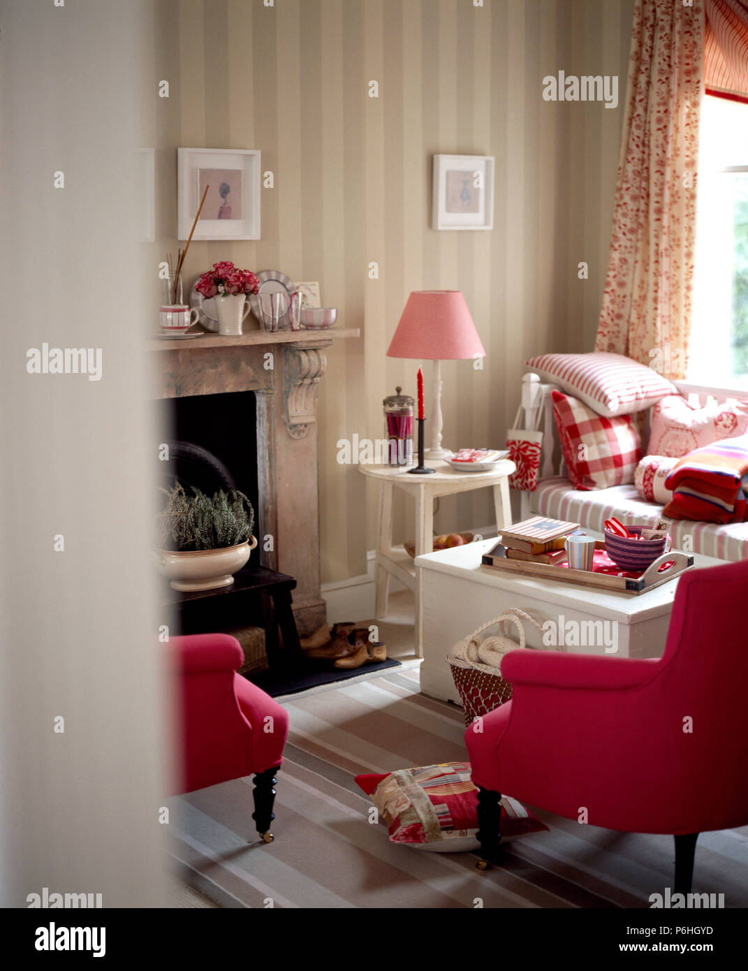 Tiefe Tinte Sessel und weiß lackierten Brust als Couchtisch im Wohnzimmer mit gestreiften Tapeten und eine blass rosa Lampe verwendet Stockfoto