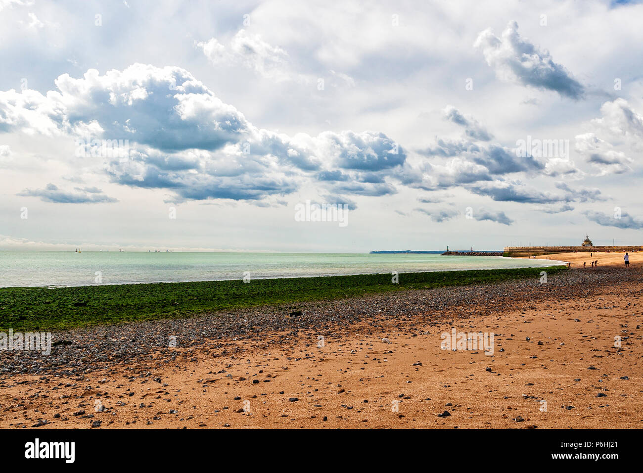 Bild der Strandszene mit sandigem Strand, grünem Algen und einer grünen Spiegelung vom Meer mit rollenden Wolken, Kent Coast, England Stockfoto