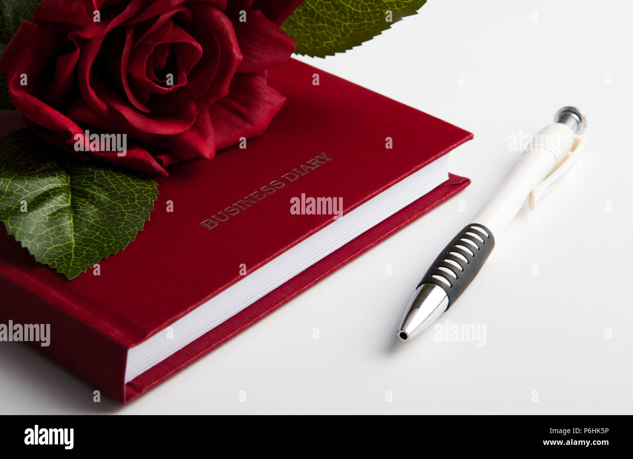 Rose Blume auf dem geschlossenen Business Tagebuch und Stift Stockfoto