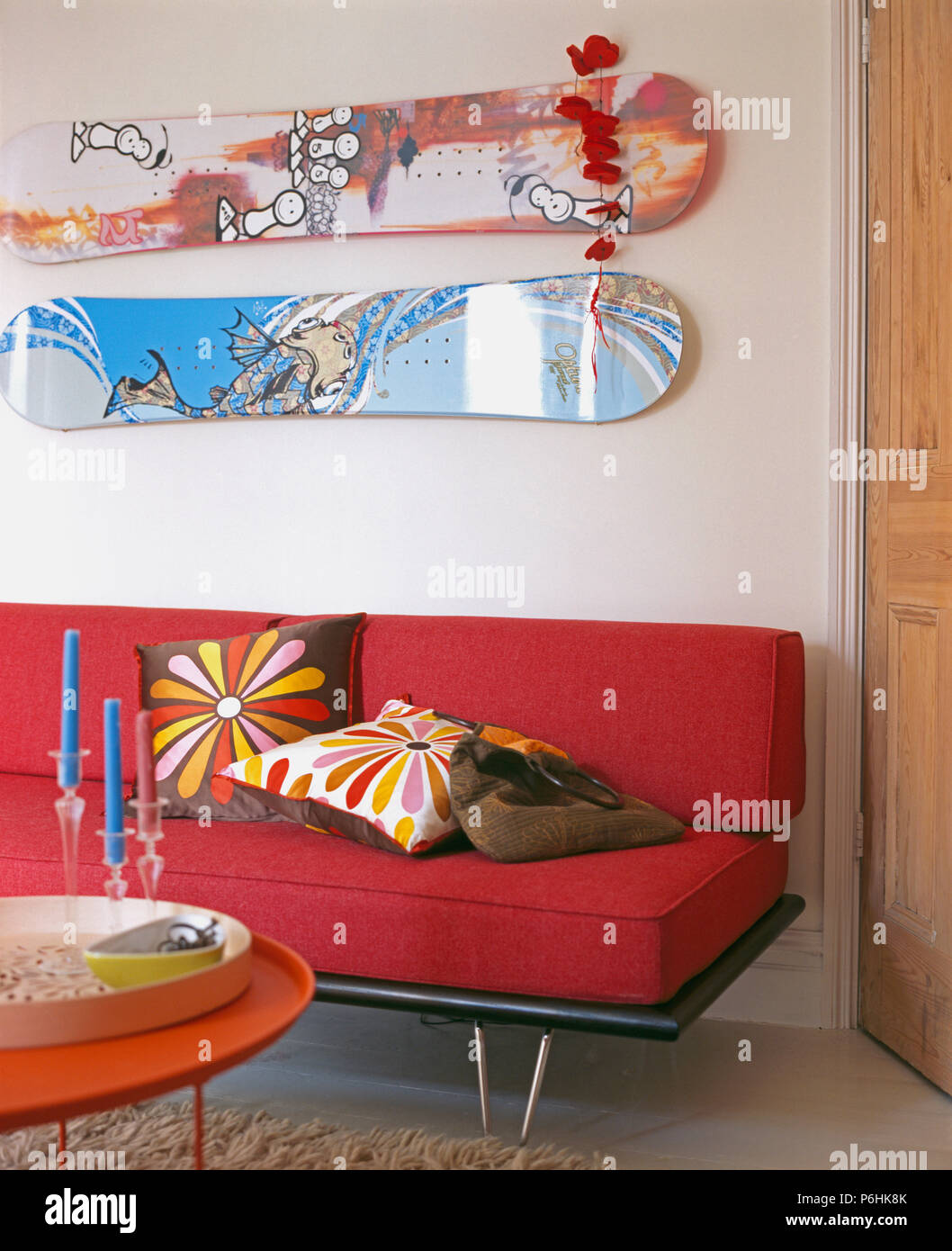 Zwei skateboards an der Wand über dem roten Sofa mit bunten Kissen in modernes weißes Wohnzimmer Stockfoto