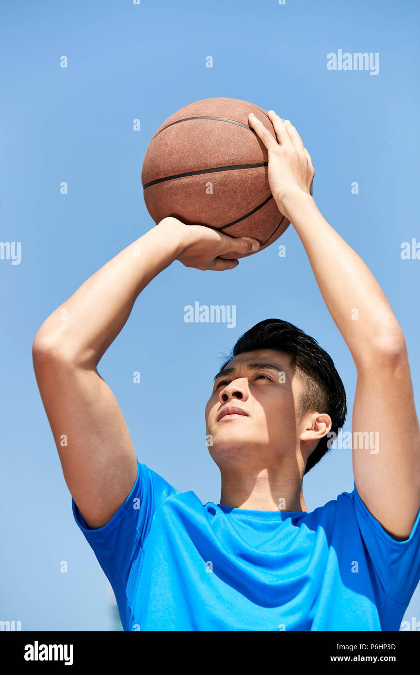 Jungen asiatischen männliche Basketball Player einen Sprungwurf gegen den blauen Himmel Hintergrund. Stockfoto