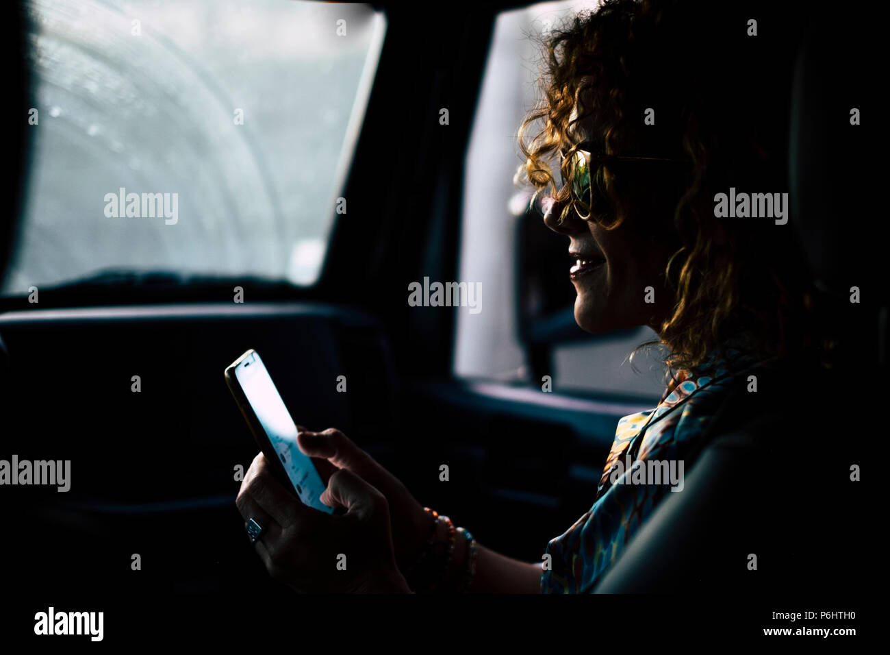 Schöne schöne Frau mittleren Alters reisen in einem Auto shile Regen. Mit einem Smartphone zu verbinden Freunde anrufen und und für die Nacht treffen zu Celeb Stockfoto