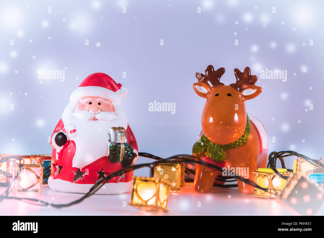 Weihnachtsmann und Rentier mit Glühbirne stehen auf weißen Hintergrund. Schneeflocke ist unten fallen. Stockfoto