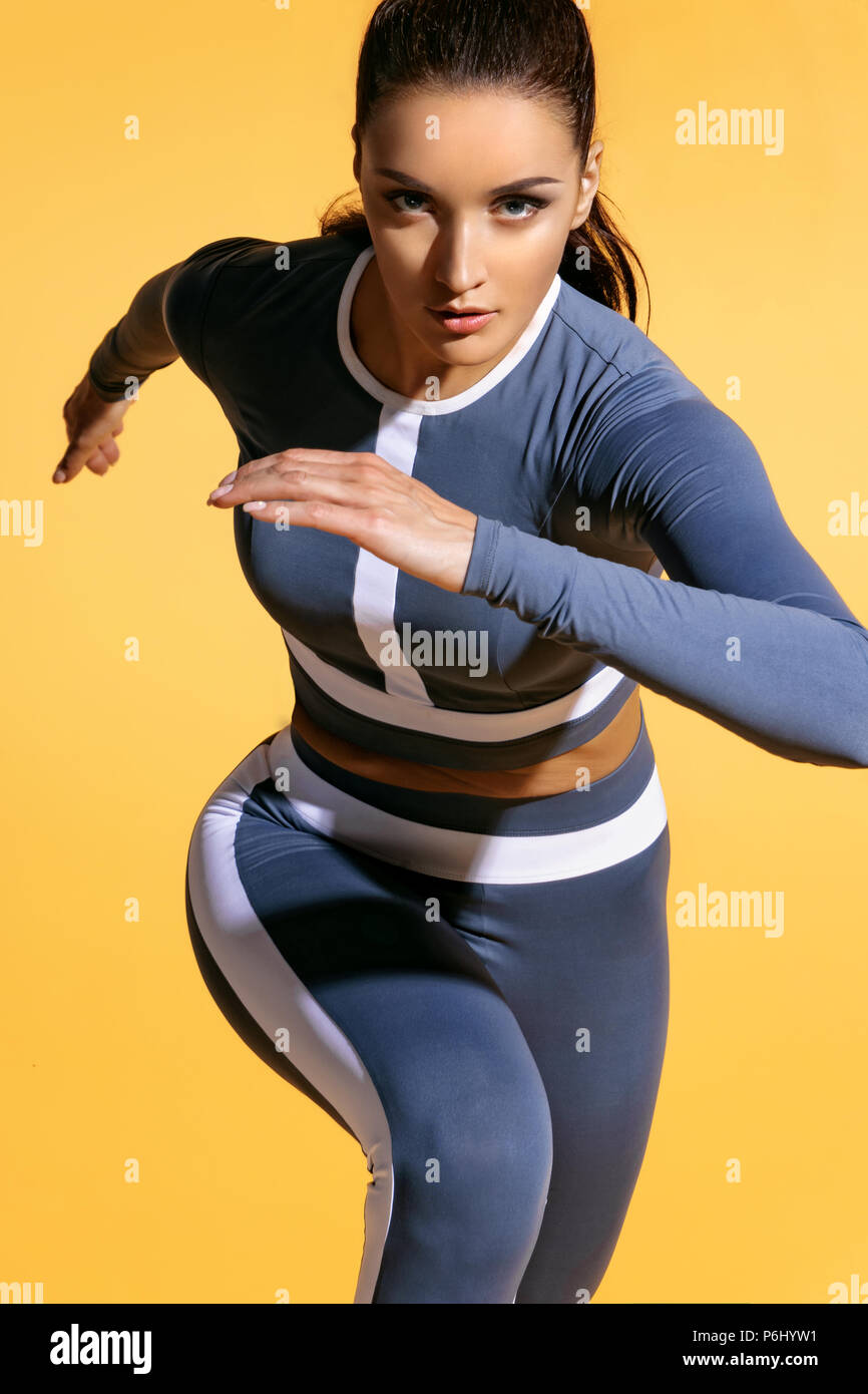 Attraktive Frau Läufer in modische Sportbekleidung auf gelben Hintergrund. Dynamische Bewegung. Close Up. Sport und eine gesunde Lebensweise Stockfoto