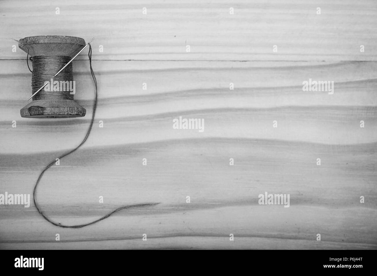 Die alte Haspel der Gewinde- und eine Nadel auf einen hölzernen Tisch in Schwarz und Weiß. Stockfoto