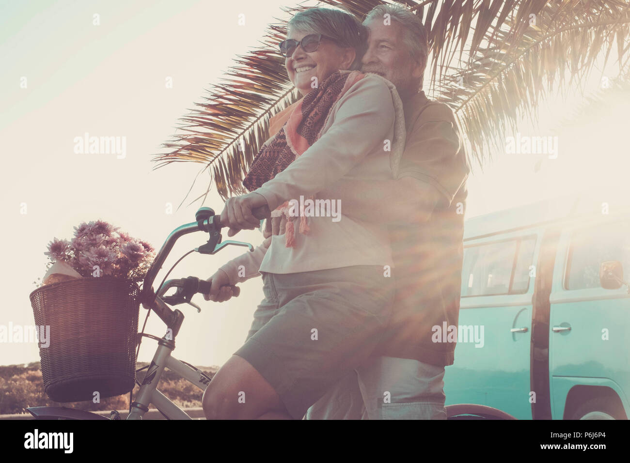 Schönen im Alter von Paar der Älteren in Urlaub gehen beide auf ein altes Fahrrad und genießen Sie den Sommer Sonnenlicht. tropisch und Vintage Retro Van im Hintergrund. Stockfoto Schönen im Alter von Paar der Älteren in Urlaub gehen beide auf ein altes Fahrrad und genießen Sie den Sommer Sonnenlicht. tropisch und Vintage Retro Van im Hintergrund. Stockfoto