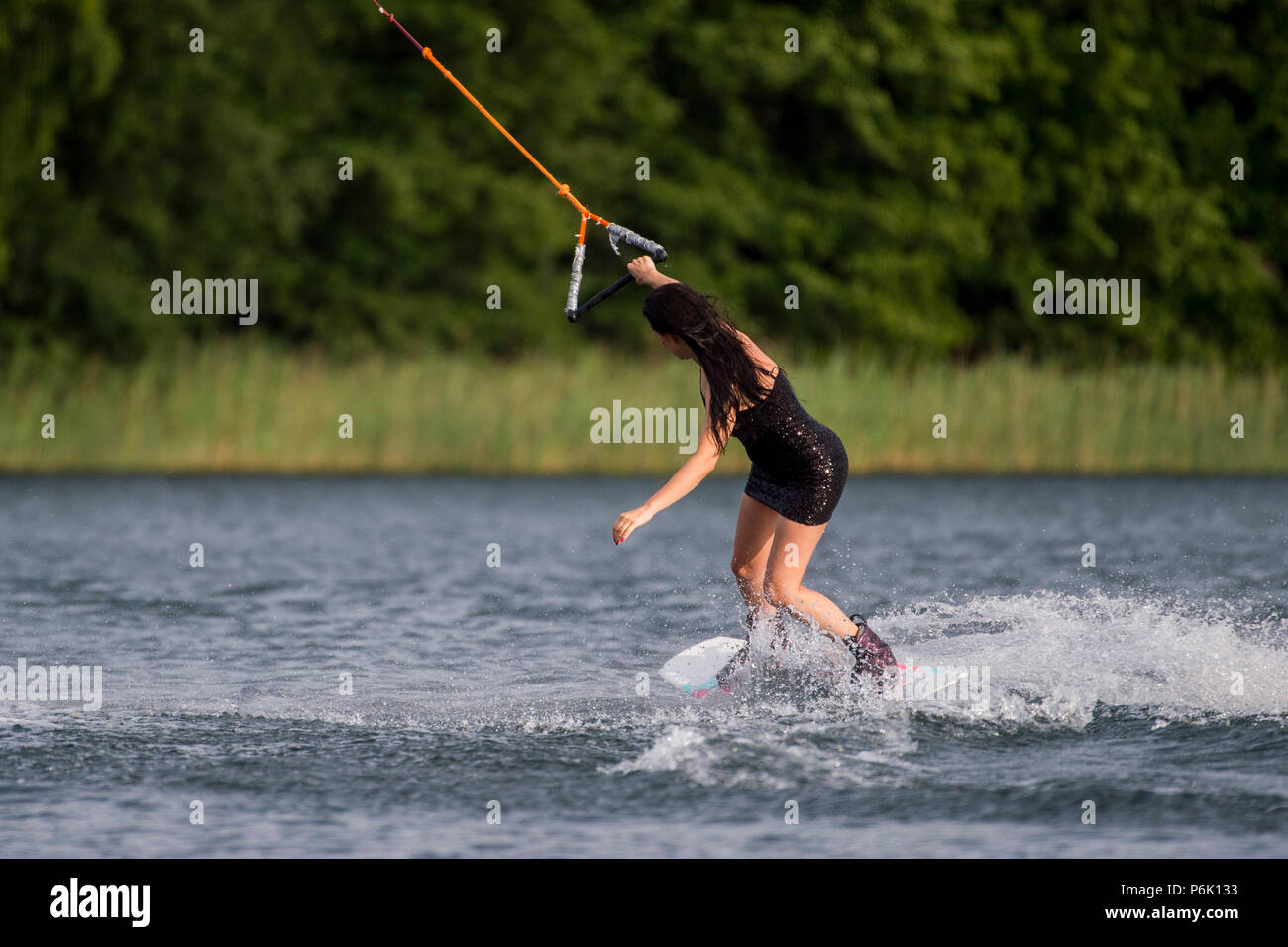 Junge hübsche schlanke Brünette Frau reiten Wakeboard in einem Sommer See Stockfoto