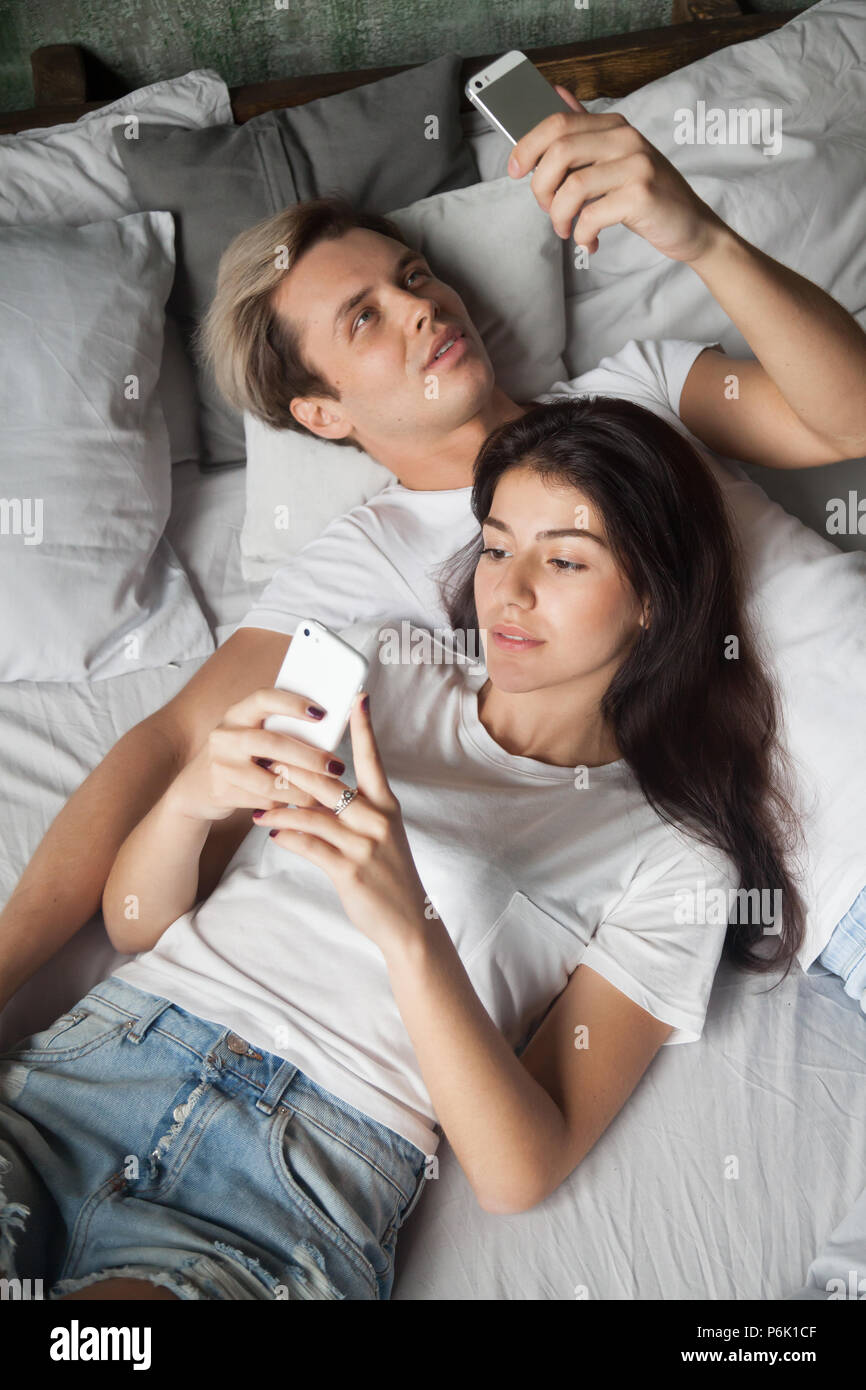 Tausendjährige paar entspannende im Bett mit Smartphones süchtig Stockfoto