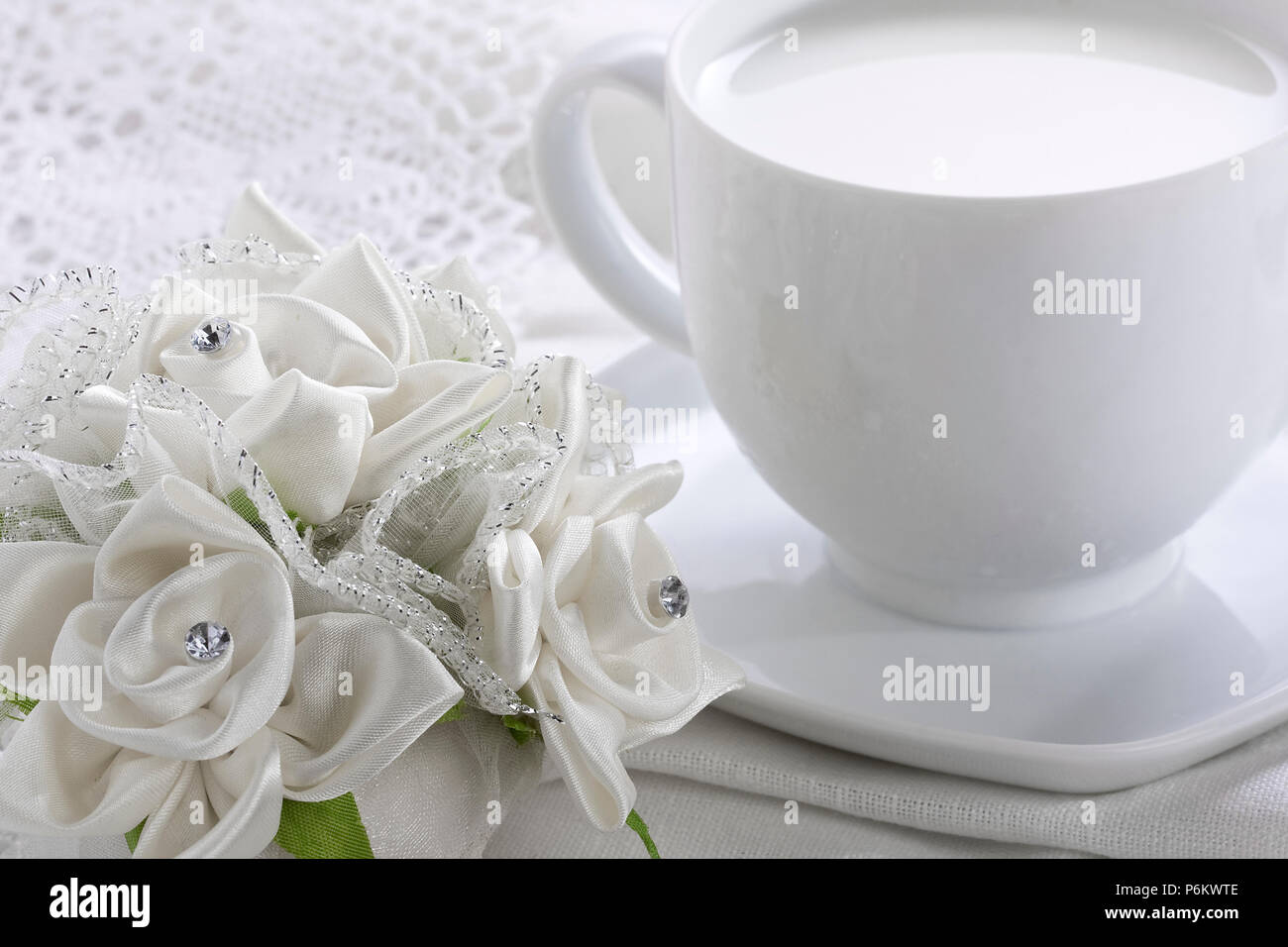 Weiße Tasse Milch und Blumenstrauß aus Rosen auf weiß Seide Häkeln tischdecke Stockfoto