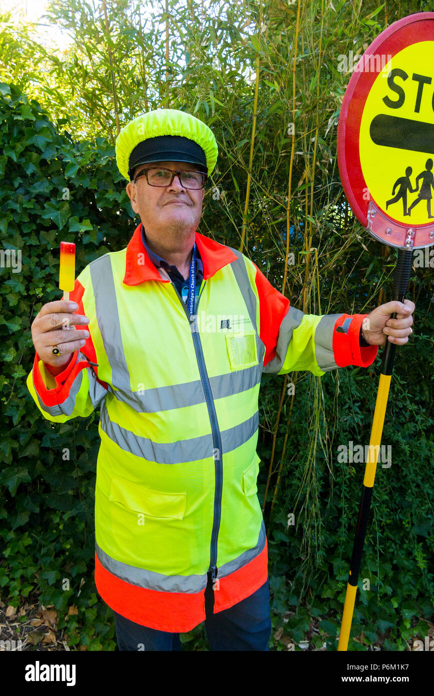 Iollipop Mann, der gerade seine Schicht an der Schule überqueren Zebrastreifen abgeschlossen hat. Er ist Abkühlung mit einem Lutscher das in derselben Farbe wie sein Outfit. England, Großbritannien Stockfoto