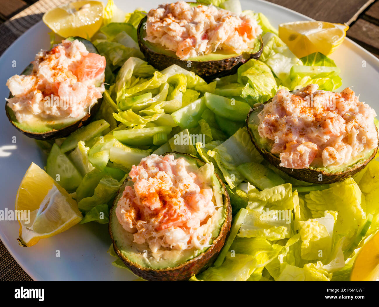 Gefüllt in Scheiben geschnittenen Avocados mit Garnelen und Krabbenfleisch auf einem Bett von Baby gem Salat mit Zitrone Keile auf Tisch im Freien in der Sonne Stockfoto
