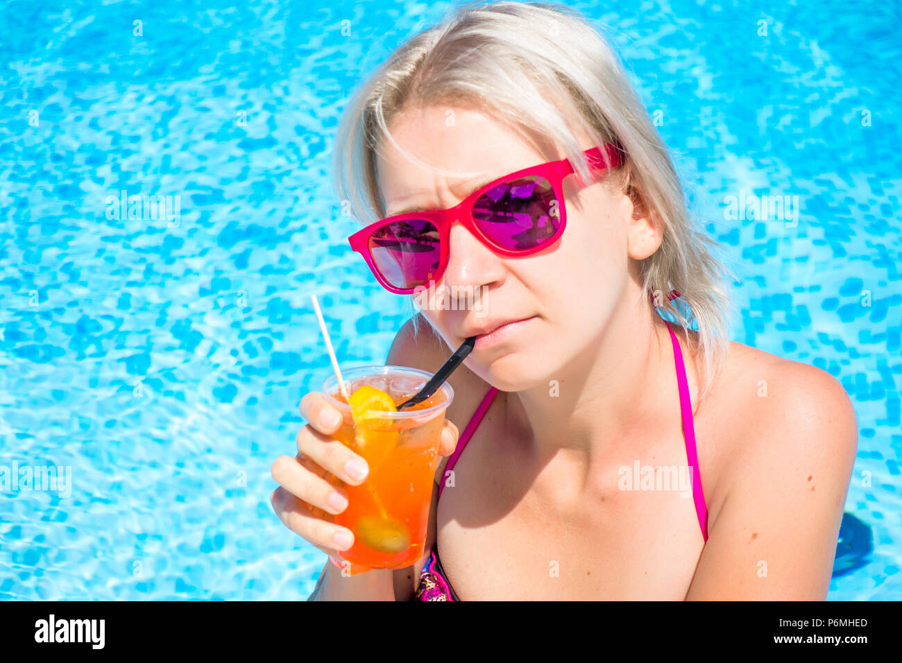 Junge blonde Frau mit Cocktail trinken im Pool. Gerne wunderschöne Frauen mit modischen Sonnenbrillen und bikini Cocktail trinken und entspannen im Freibad Stockfoto
