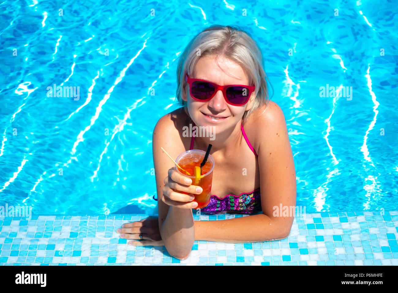 Junge blonde Frau mit Cocktail trinken im Pool. Gerne wunderschöne Frauen mit modischen Sonnenbrillen und bikini Cocktail trinken und entspannen im Freibad Stockfoto