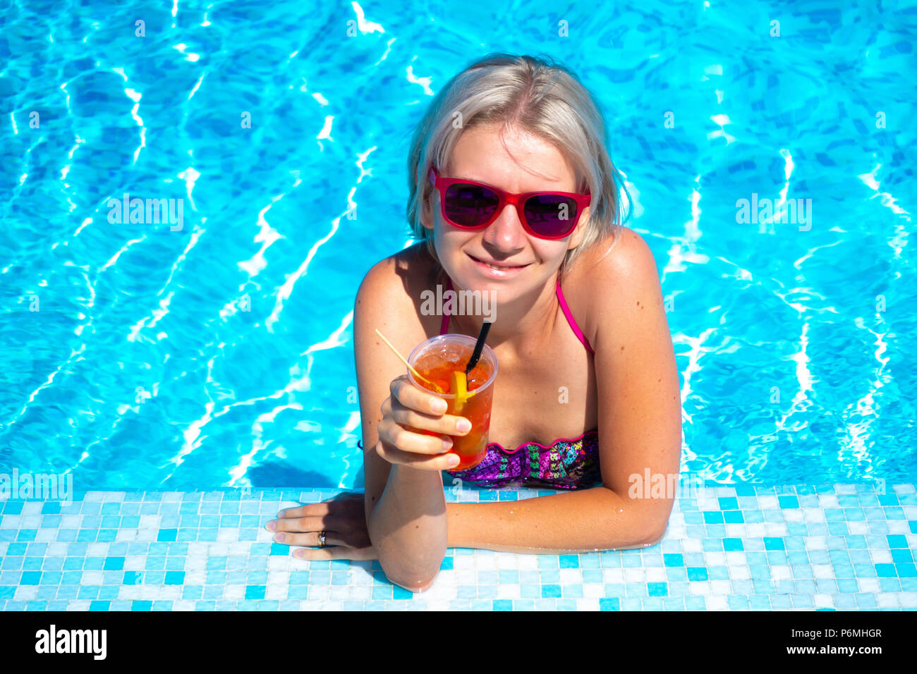 Junge blonde Frau mit Cocktail trinken im Pool. Gerne wunderschöne Frauen mit modischen Sonnenbrillen und bikini Cocktail trinken und entspannen im Freibad Stockfoto